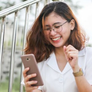 A woman in white button-up shirt holding silver iPhone 6. The feeling of happiness having conversation with your friend, or when visiting a Cadent website with a mobile responsive layout